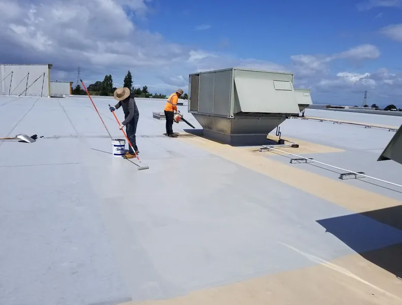 Crew rolling elastomeric coating across a large flat roof