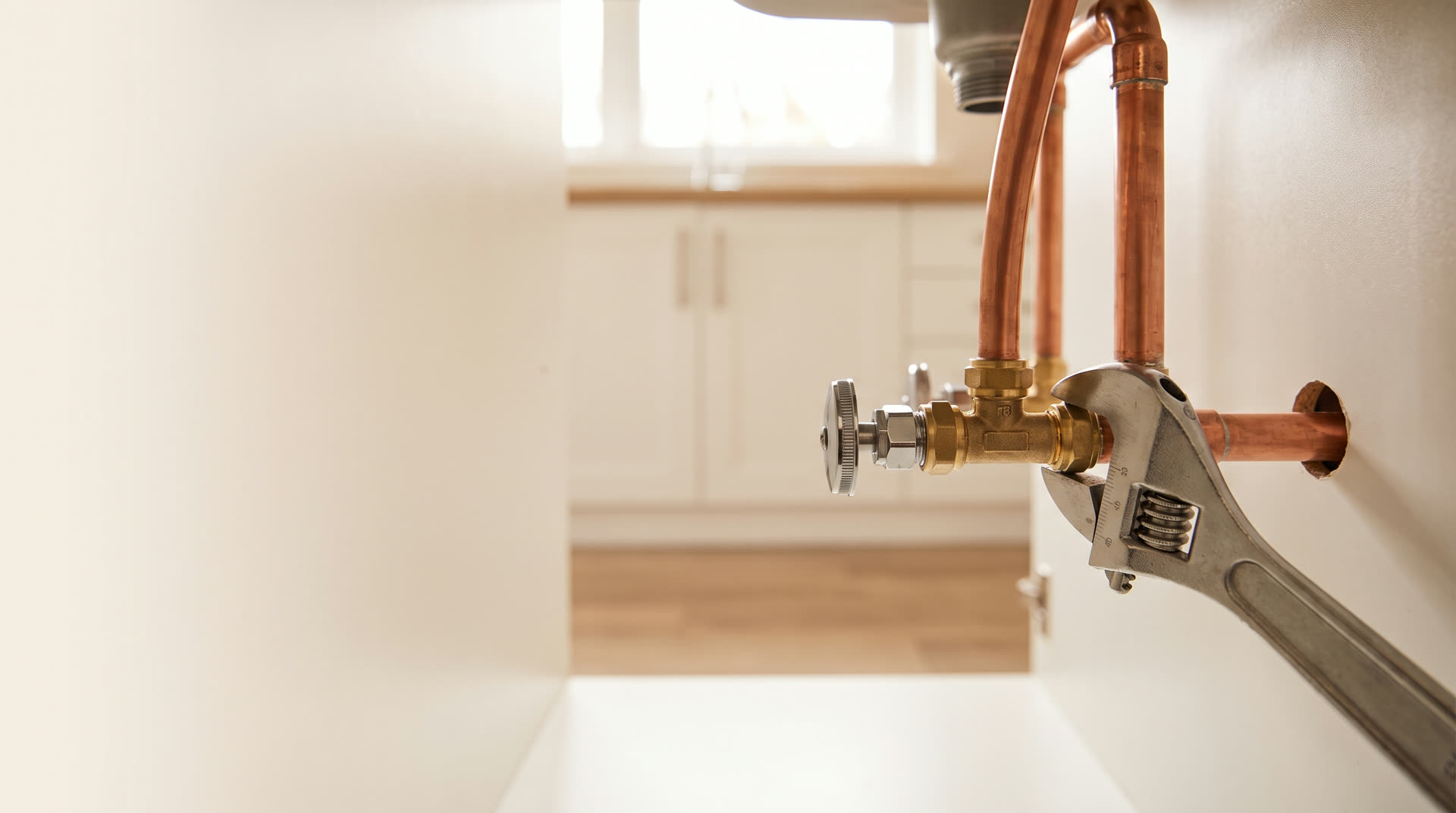Copper pipework and a wrench under a kitchen sink